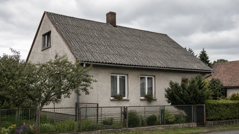 Stará šedá vlnitá eternitová střecha rodinného domu s patrnou degradací a mechem
